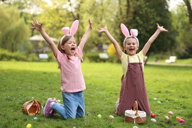 Photo of Easter celebration. Cute little girls in bunny ears hunting eggs outdoors