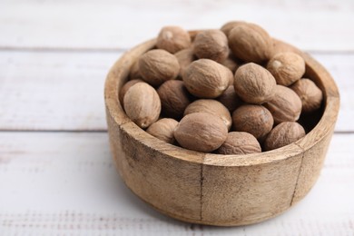 Photo of Whole nutmegs in bowl on light wooden table, closeup. Space for text