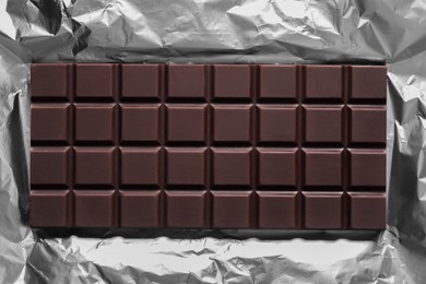 Photo of Delicious dark chocolate bar on foil, top view