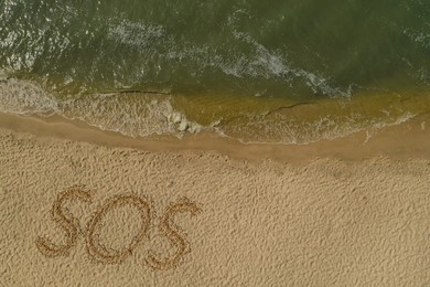 Image of SOS message drawn on sandy beach near sea, above view