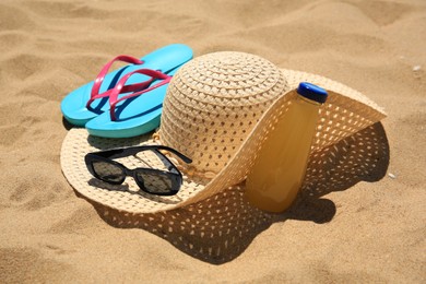 Photo of Straw hat, sunglasses, flip flops and refreshing drink on sand. Beach accessories