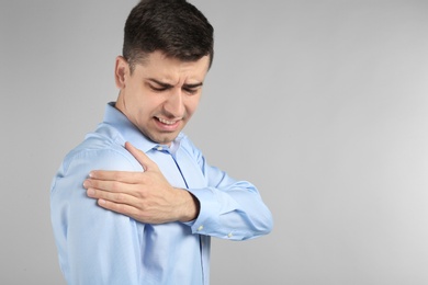 Photo of Young man suffering from pain in shoulder on light background