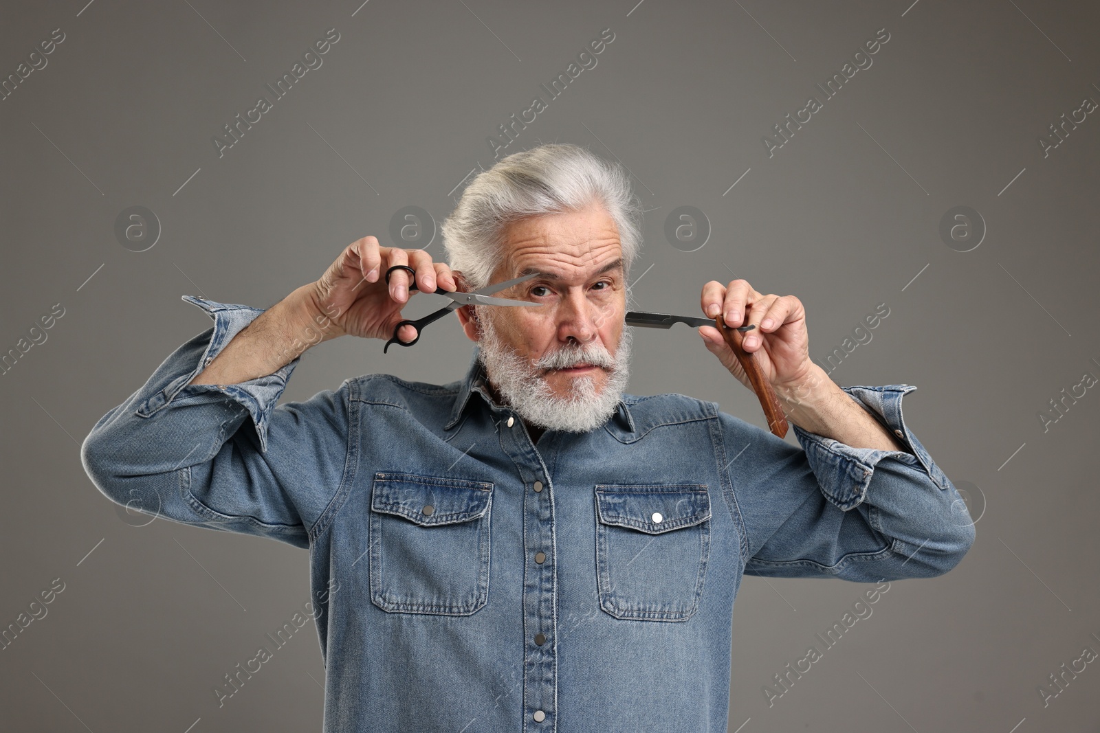 Photo of Senior man with mustache holding blade and scissors on grey background