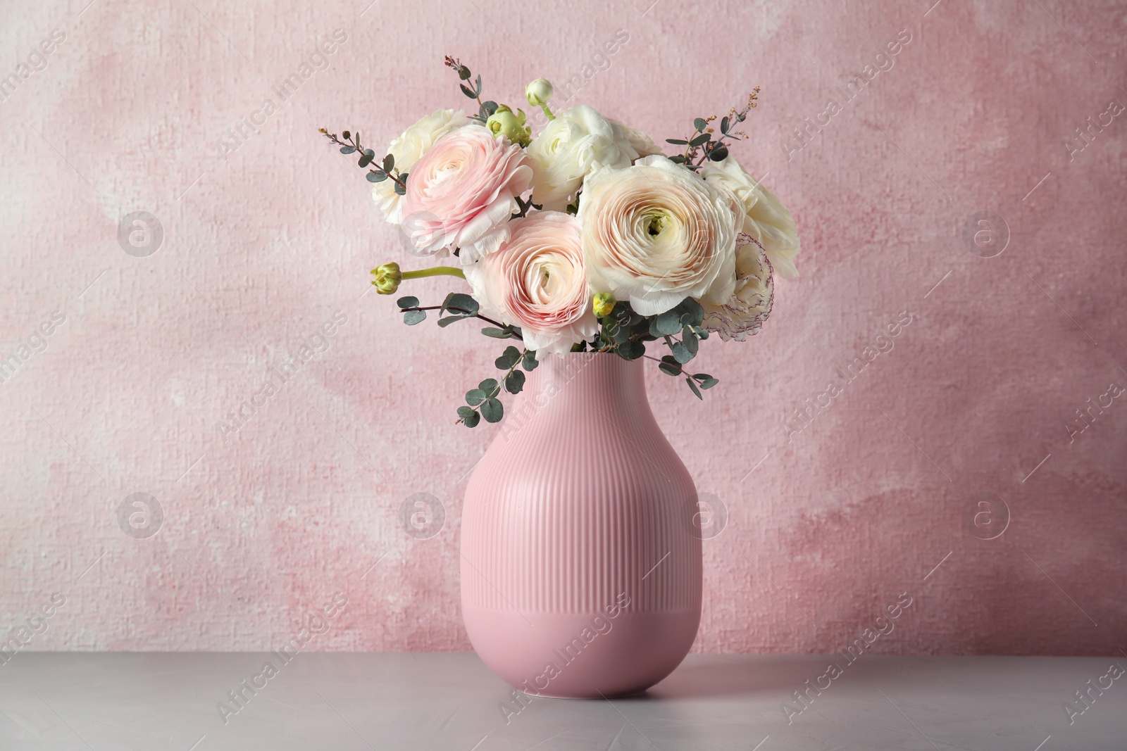 Photo of Vase with beautiful spring ranunculus flowers on table against color background