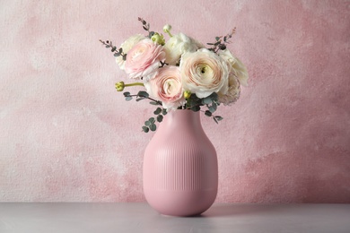 Vase with beautiful spring ranunculus flowers on table against color background