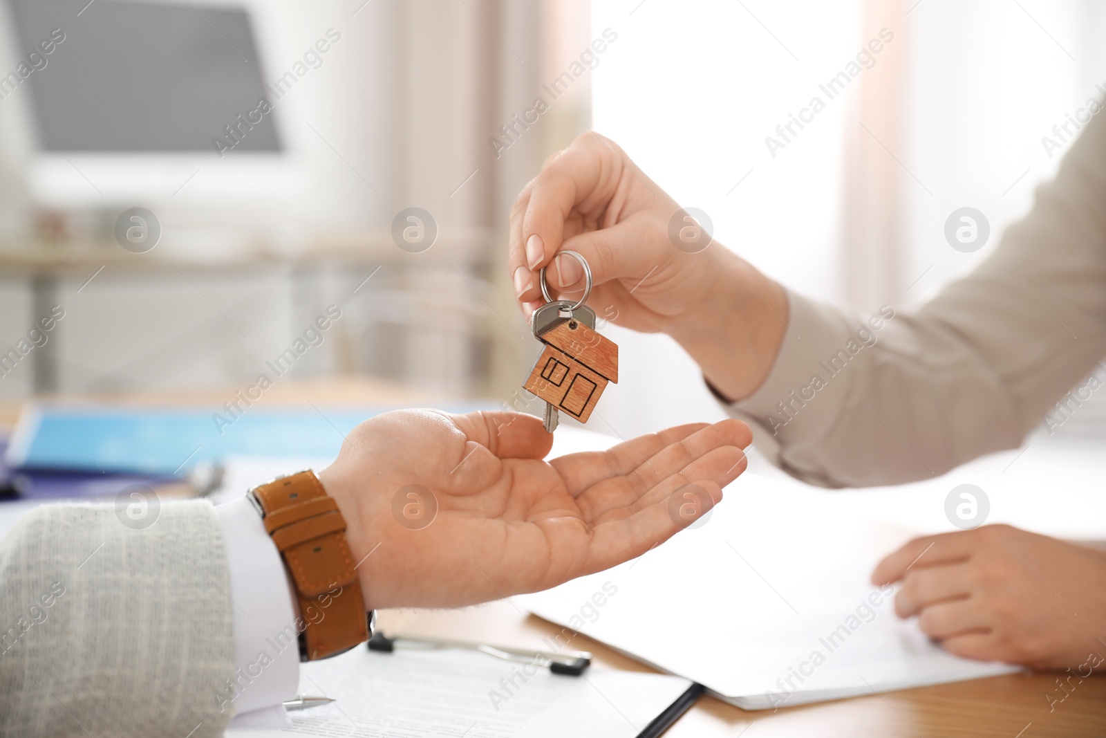 Photo of Real estate agent giving key with trinket to client in office, closeup