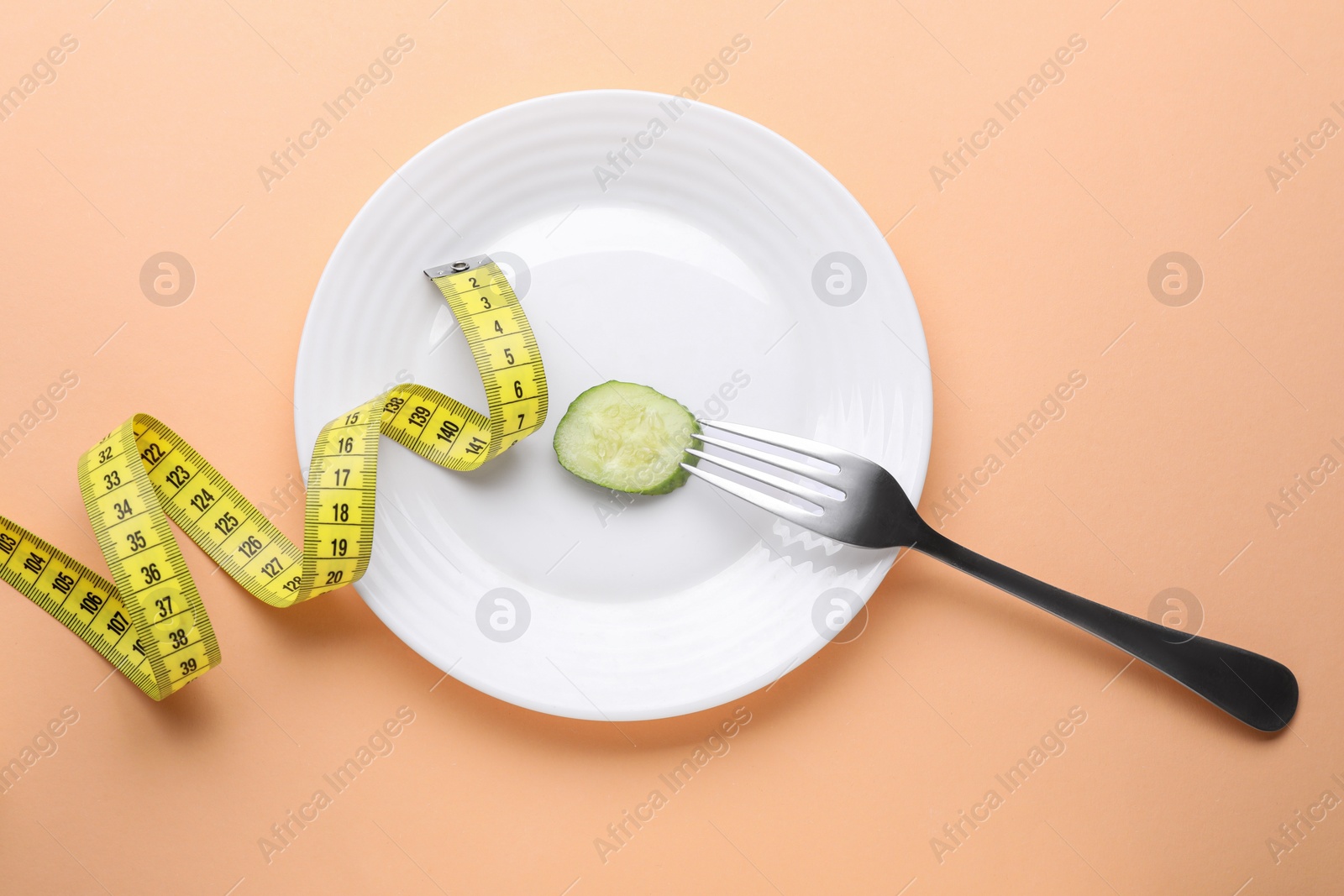 Photo of Plate with cucumber slice, fork and measuring tape on pale orange background, flat lay. Diet concept