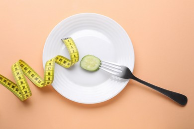 Plate with cucumber slice, fork and measuring tape on pale orange background, flat lay. Diet concept