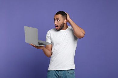 Photo of Surprised young man with laptop on lilac background