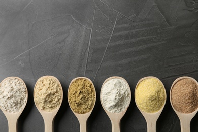 Spoons with different types of flour on grey background, top view. Space for text