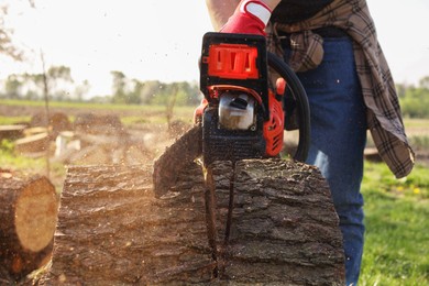 Photo of Man sawing wooden log outdoors, closeup view