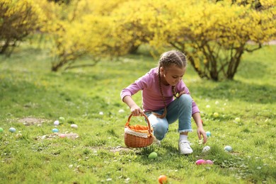 Photo of Easter celebration. Cute little girl hunting eggs outdoors, space for text