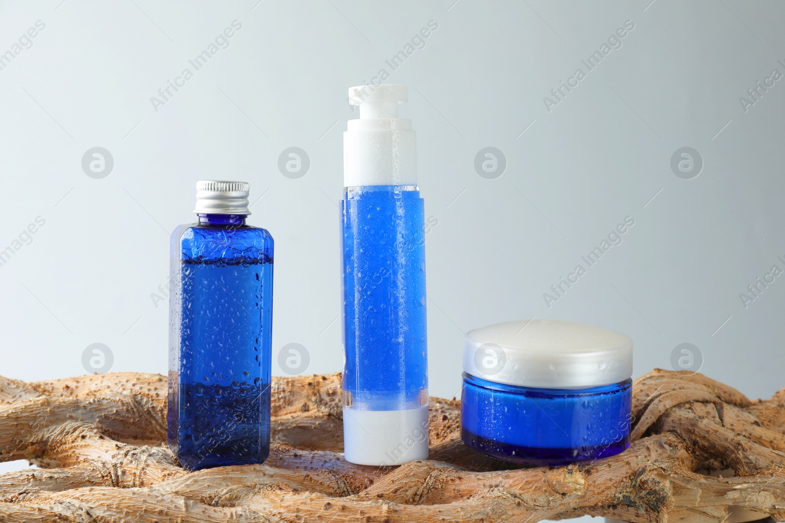 Photo of Set of cosmetic products on wooden branch against light grey background