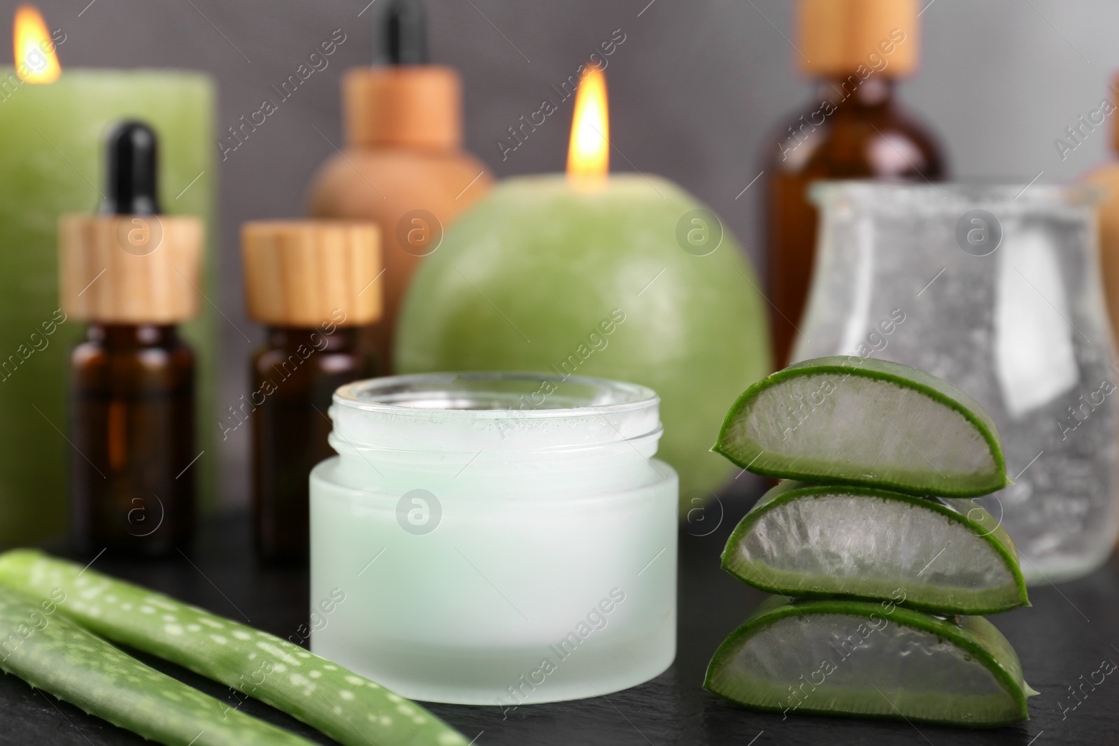 Photo of Jar of natural gel and aloe vera leaves near cosmetic products on black table, closeup