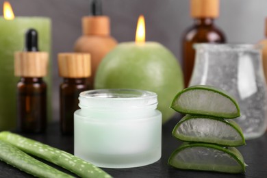 Photo of Jar of natural gel and aloe vera leaves near cosmetic products on black table, closeup