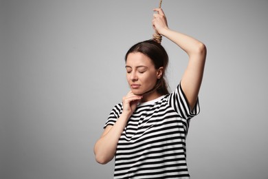 Photo of Depressed woman with rope noose on neck against light grey background