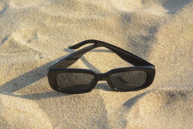 Photo of Stylish sunglasses on sandy beach, closeup. Space for text