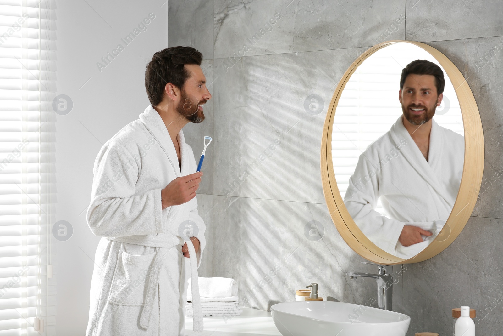 Photo of Happy man with tongue cleaner near mirror in bathroom