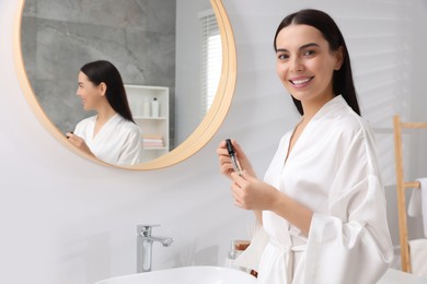 Beautiful young woman with gel for eyelashes near mirror in bathroom