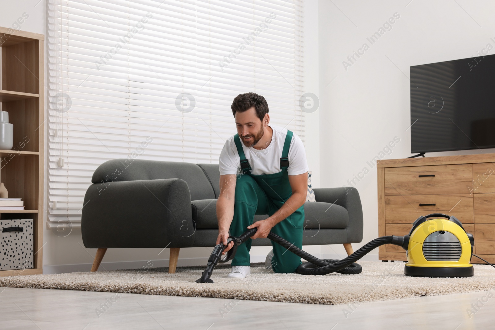 Photo of Dry cleaner's employee hoovering carpet with vacuum cleaner in room