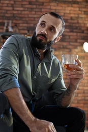 Photo of Handsome man holding glass of whiskey indoors