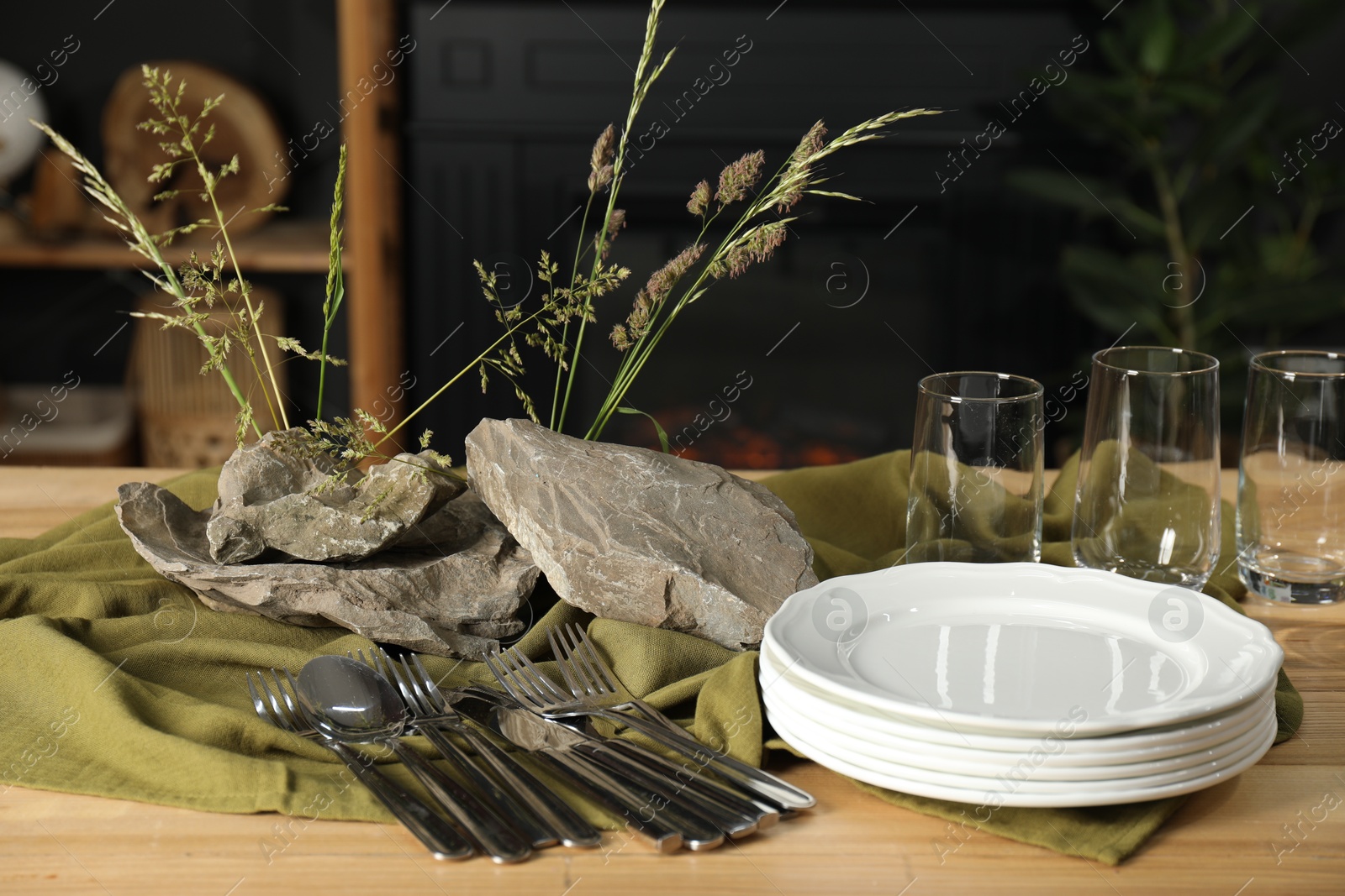 Photo of Clean dishes, stones and plants on wooden table in stylish dining room