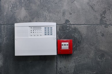 Photo of Fire alarm push button and house security system control panel on grey wall, space for text
