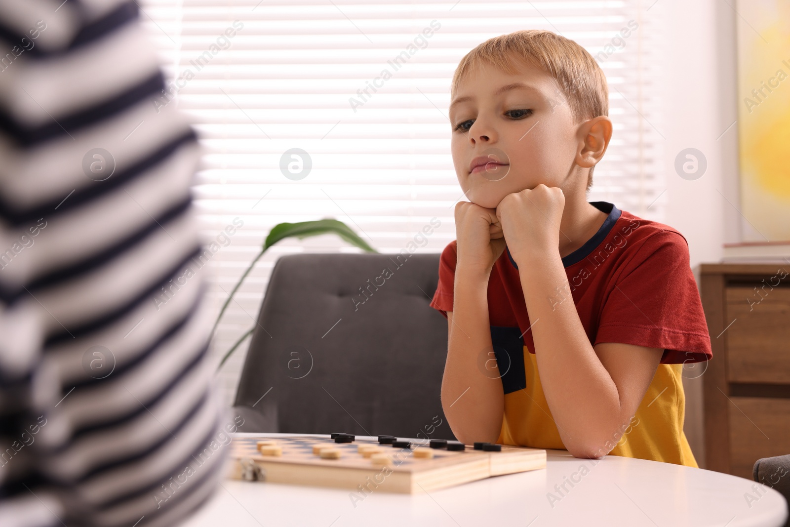 Photo of Cute boy playing checkers at coffee table indoors