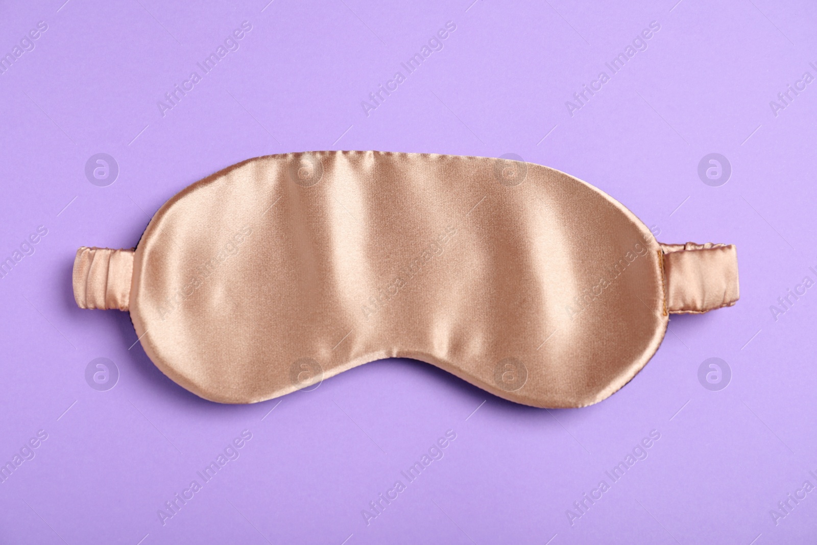 Photo of Beige sleeping mask on violet background, top view. Bedtime accessory