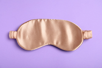 Photo of Beige sleeping mask on violet background, top view. Bedtime accessory