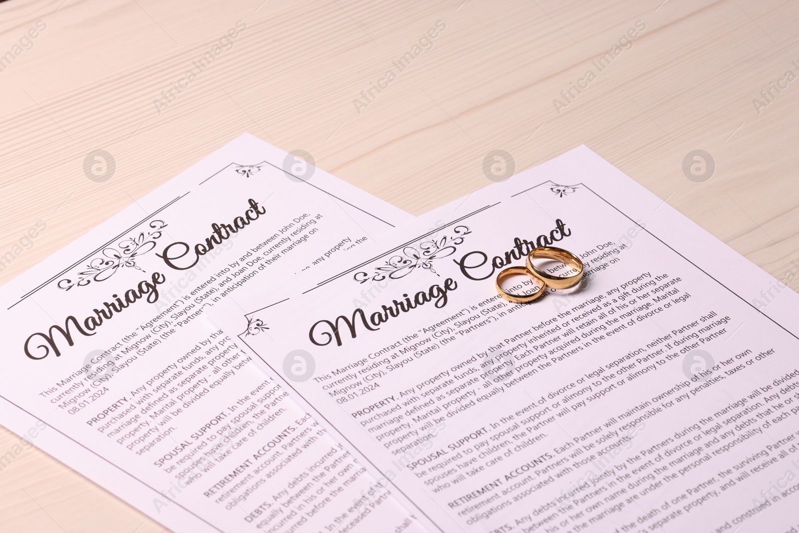 Photo of Marriage contracts and gold rings on light wooden table, closeup