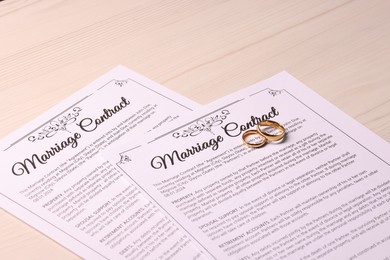 Marriage contracts and gold rings on light wooden table, closeup