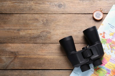 Photo of Modern binoculars, map and compass on wooden table, flat lay. Space for text