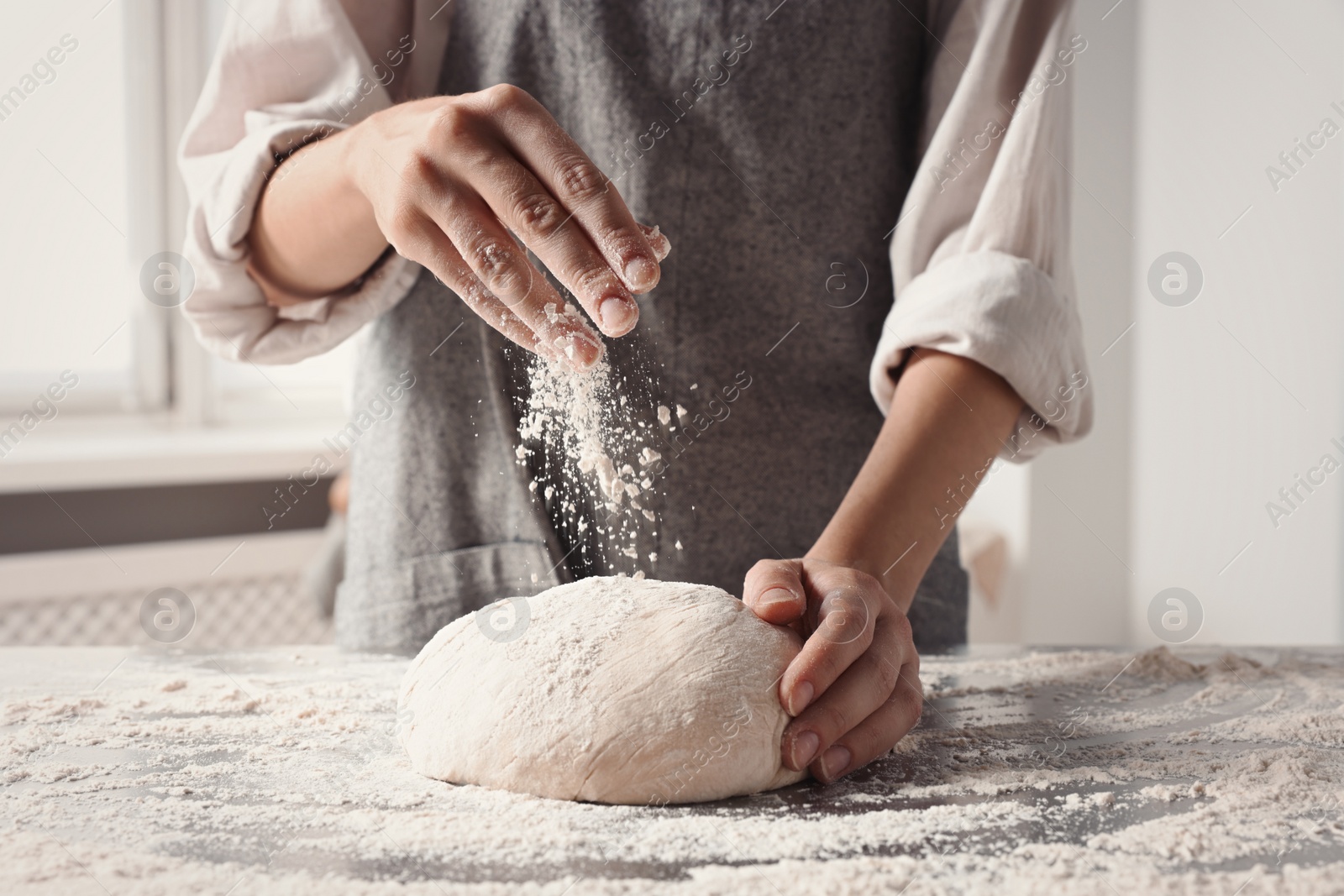 Photo of Woman sprinkling flour over dough at table in kitchen, closeup