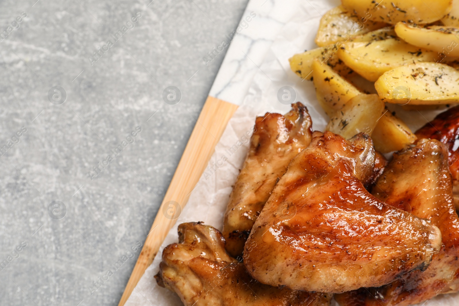 Photo of Delicious fried chicken wings served with baked potatoes on table, top view. Space for text