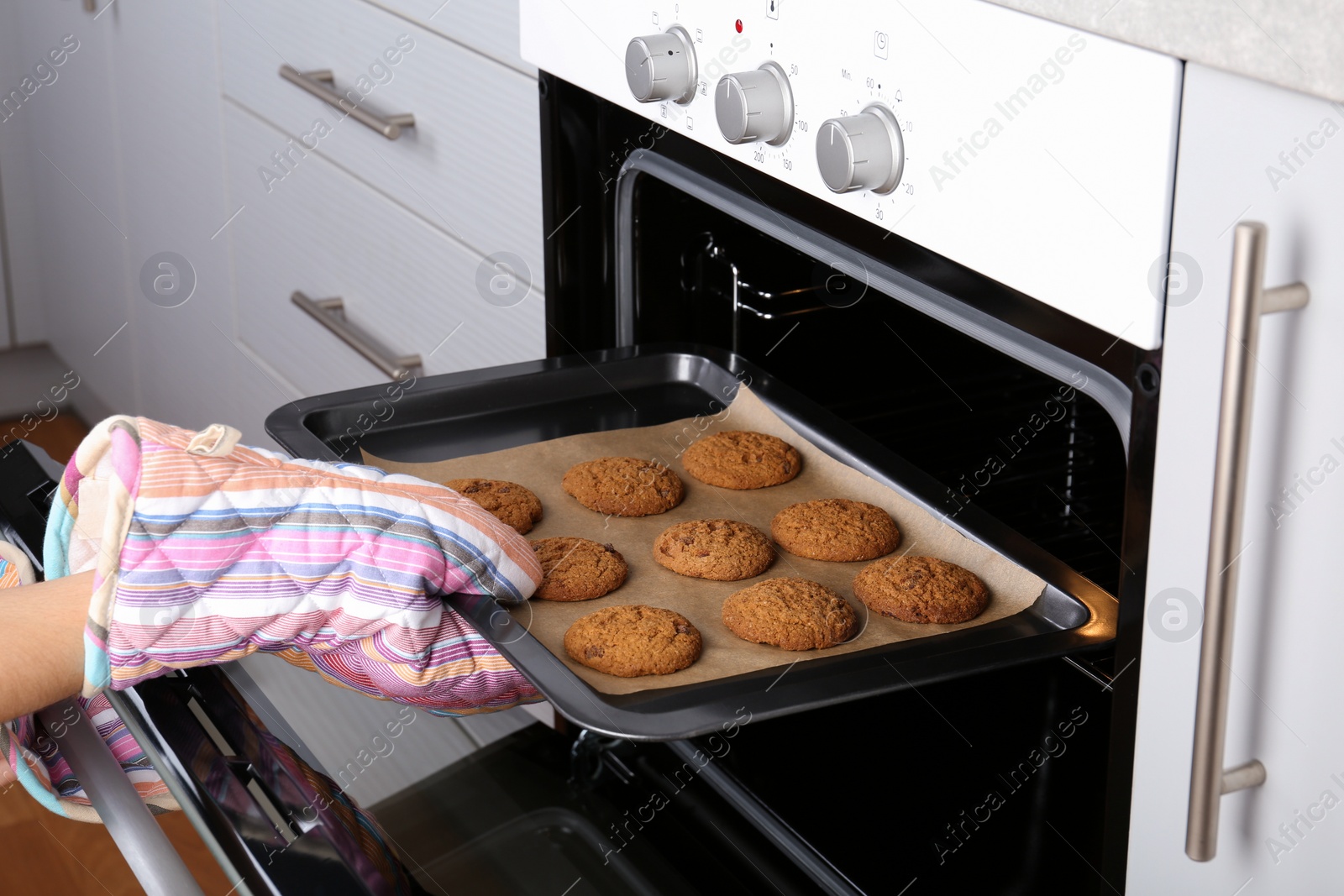 Photo of Woman taking baking tray with delicious cookies out of electric oven in kitchen, closeup