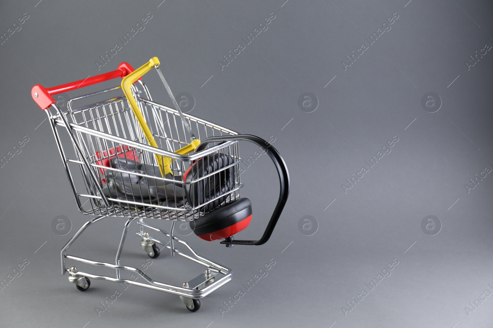 Photo of Small shopping cart with hacksaw, gloves and headphones on grey background. Space for text