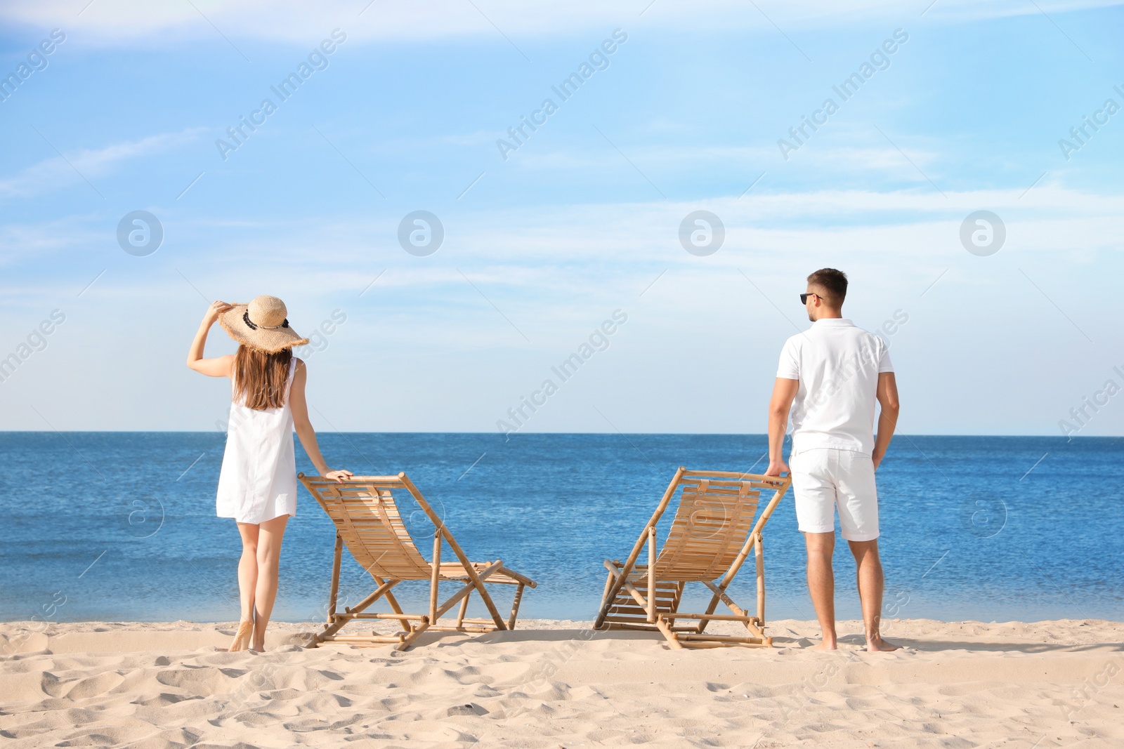 Photo of Young couple near deck chairs on sandy beach