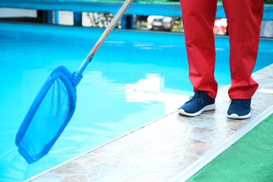 Photo of Male worker cleaning outdoor pool with scoop net