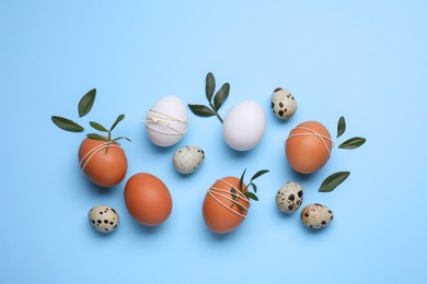 Photo of Beautifully decorated Easter eggs and green leaves on light blue background, flat lay