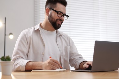 Photo of Young man in glasses watching webinar at table in room