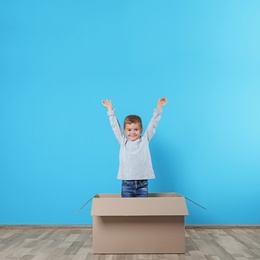 Photo of Cute little boy playing with cardboard box near color wall