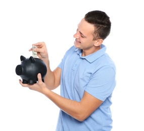 Young man putting money into piggy bank on white background