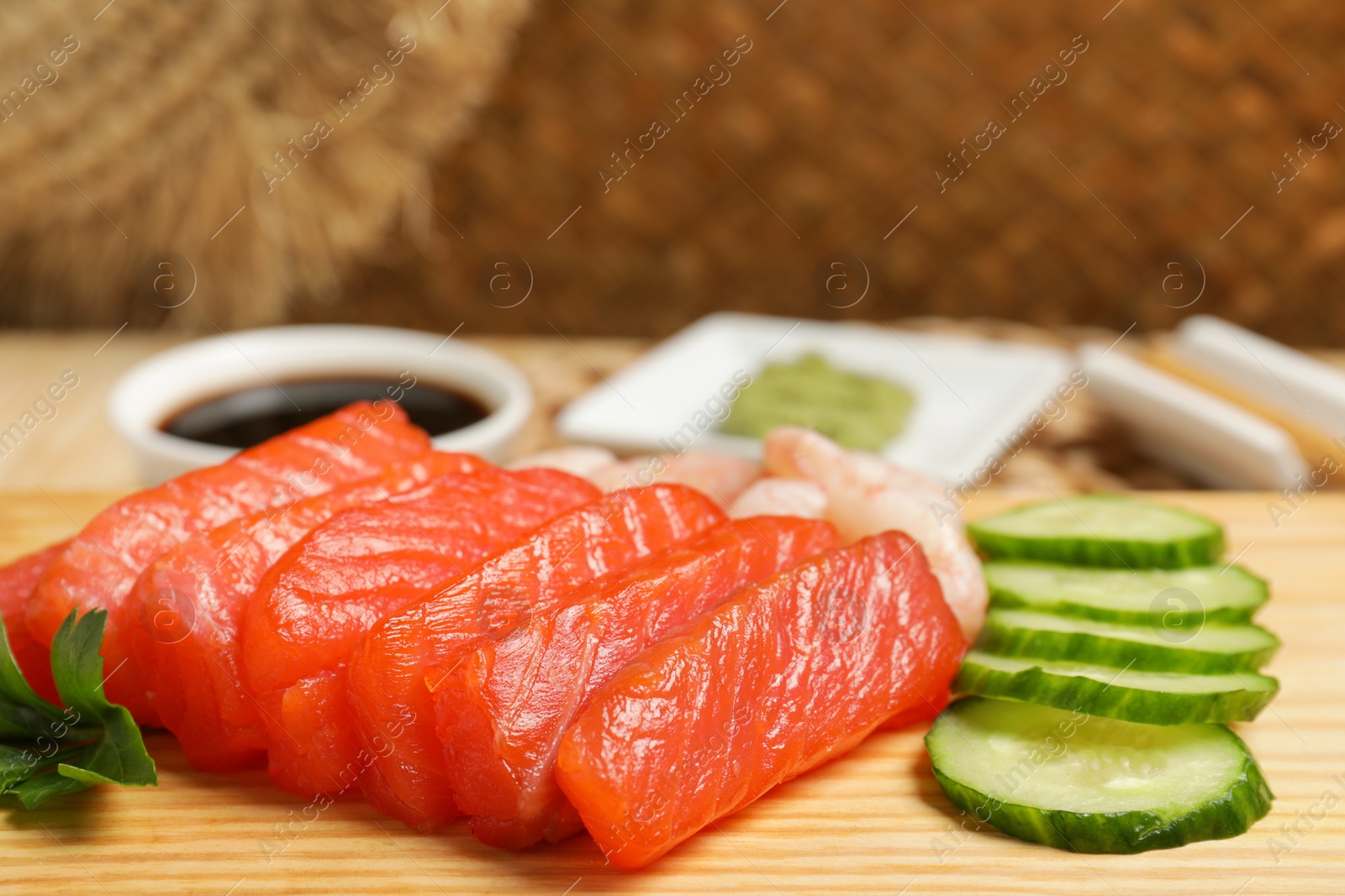 Photo of Delicious sashimi set of salmon and shrimps served with cucumbers on wooden board, closeup