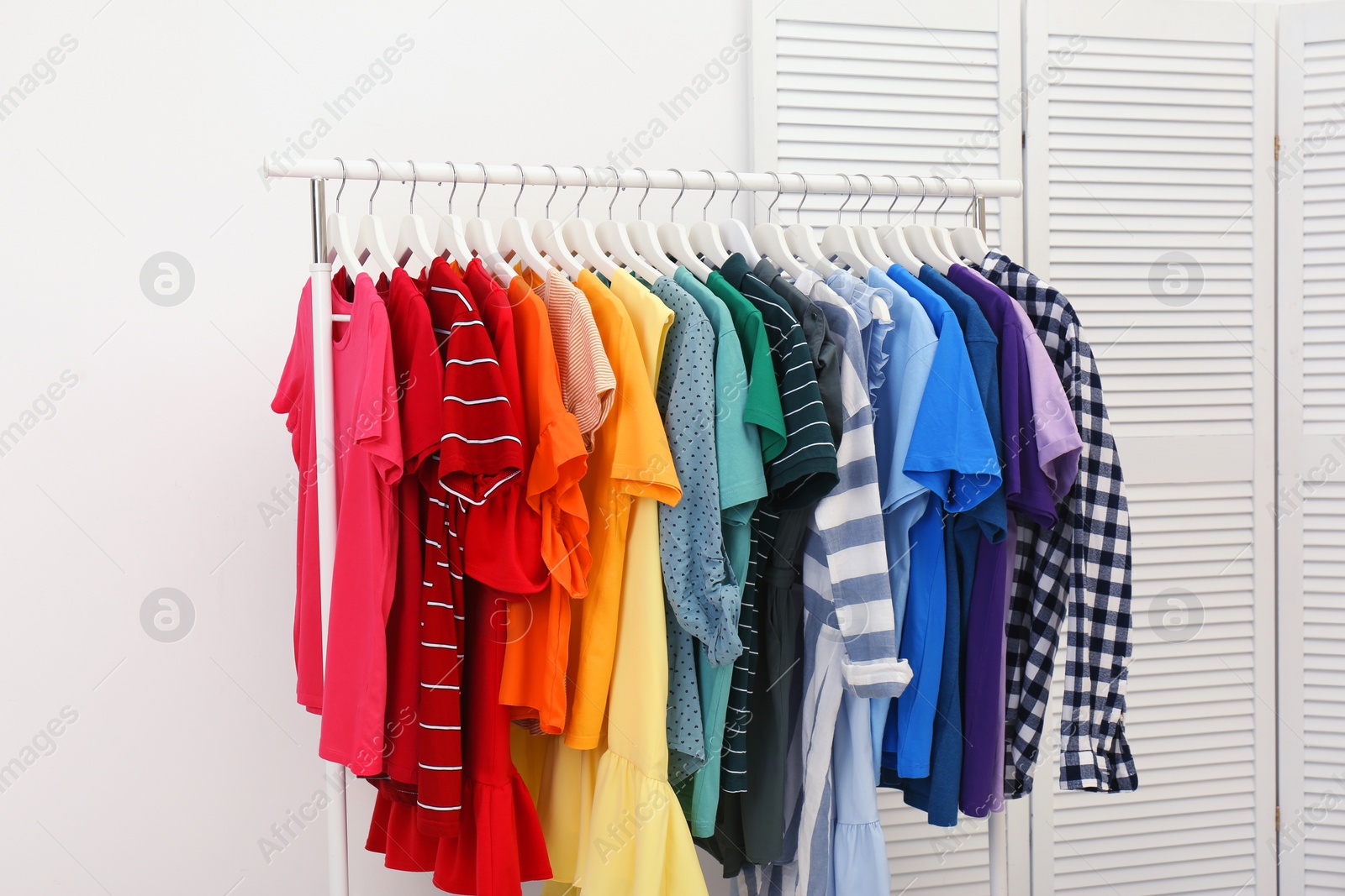 Photo of Rack with bright clothes in room. Rainbow colors