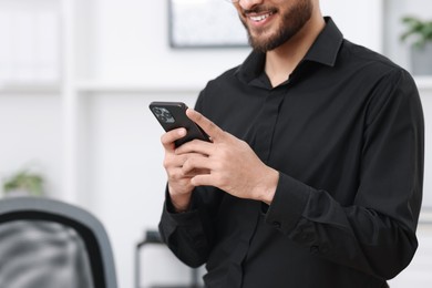 Man using smartphone in office, closeup. Space for text