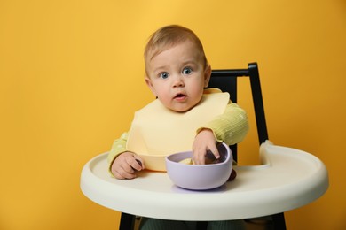 Photo of Cute little baby wearing bib while eating on yellow background