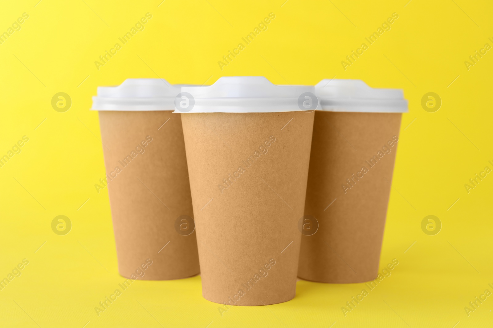 Photo of Paper cups with white lids on yellow background. Coffee to go