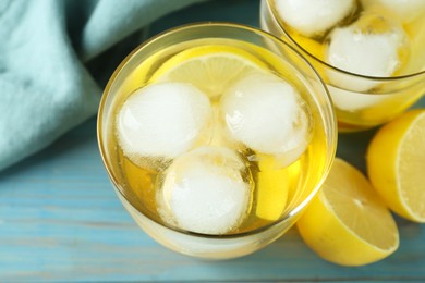 Delicious cocktails with lemon and ice balls on light blue wooden table, above view