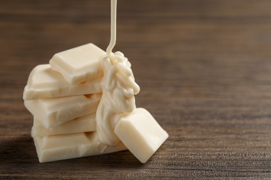 Photo of Pouring tasty white chocolate paste onto pieces on wooden table, closeup. Space for text